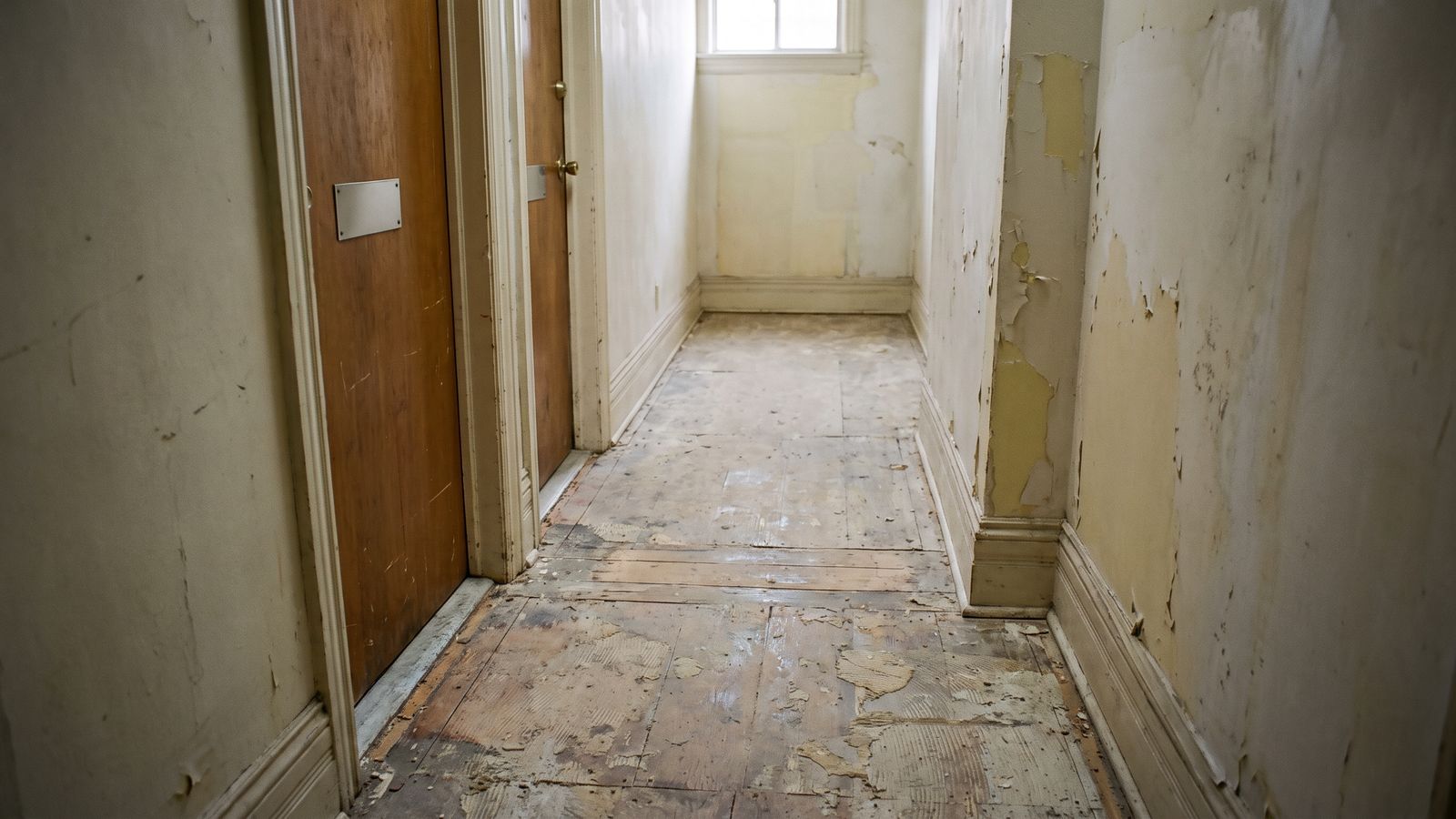 Two closed unit doors along a bare subfloor corridor with the finish flooring removed