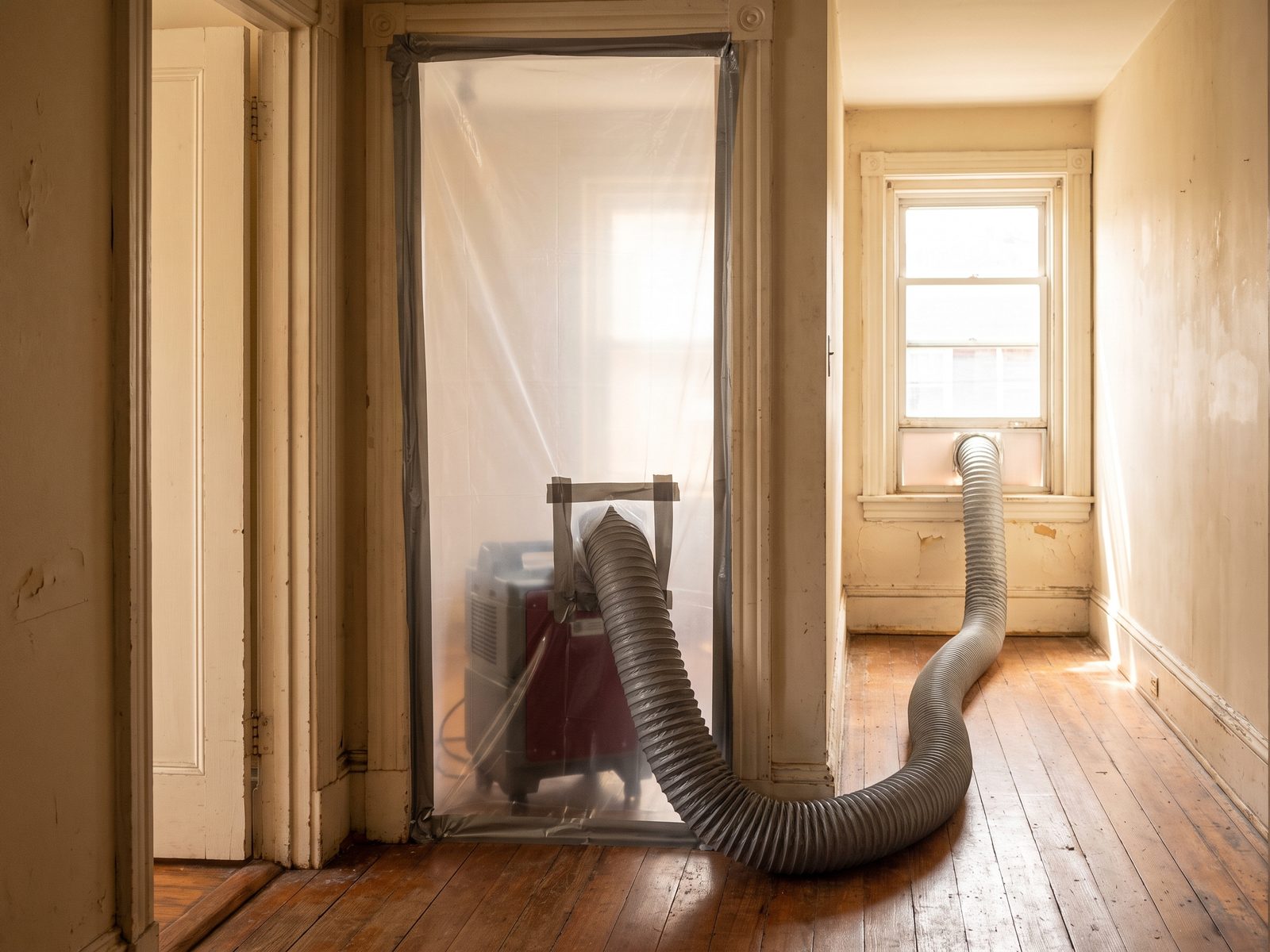 Containment and negative air in a row-house hallway Sealed plastic containment across a row-house hallway doorway with a flexible exhaust duct running out through a window.