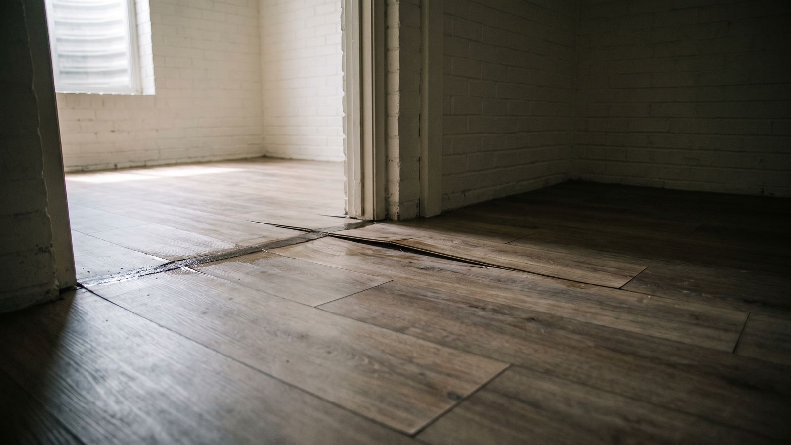 Laminate flooring lifted at a doorway threshold Laminate plank floor lifted and separated at a doorway threshold after English basement water damage in a DC lower unit