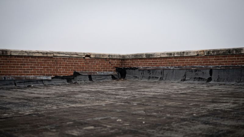 Cracked stone coping and split base flashing on a brick parapet, a common flat roof leak source