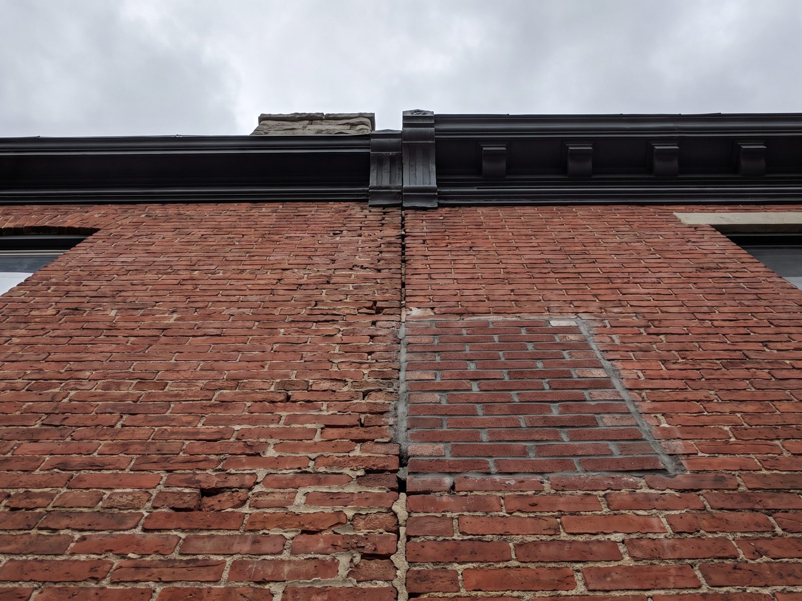 Shared brick wall between two row houses Weathered mortar joints along the shared brick wall line between two attached row houses seen from below.