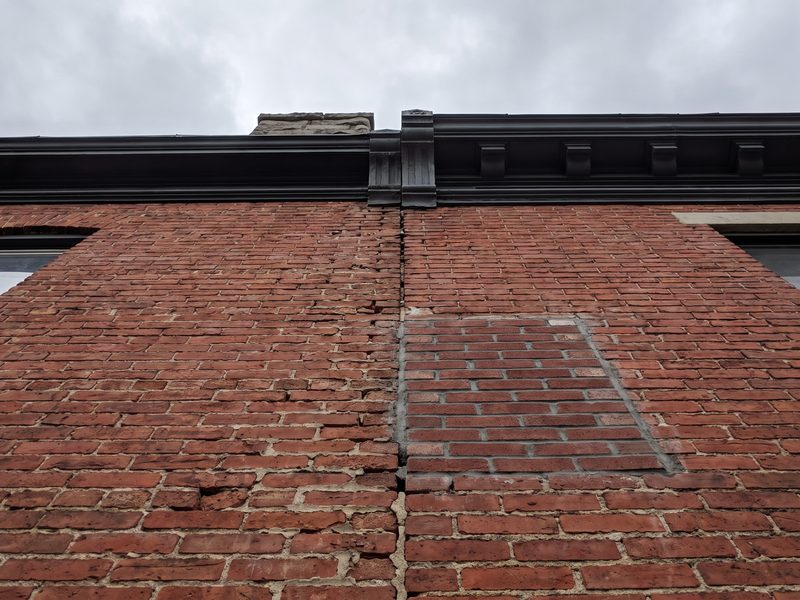 Weathered mortar joints along the shared brick wall line between two attached row houses seen from below.