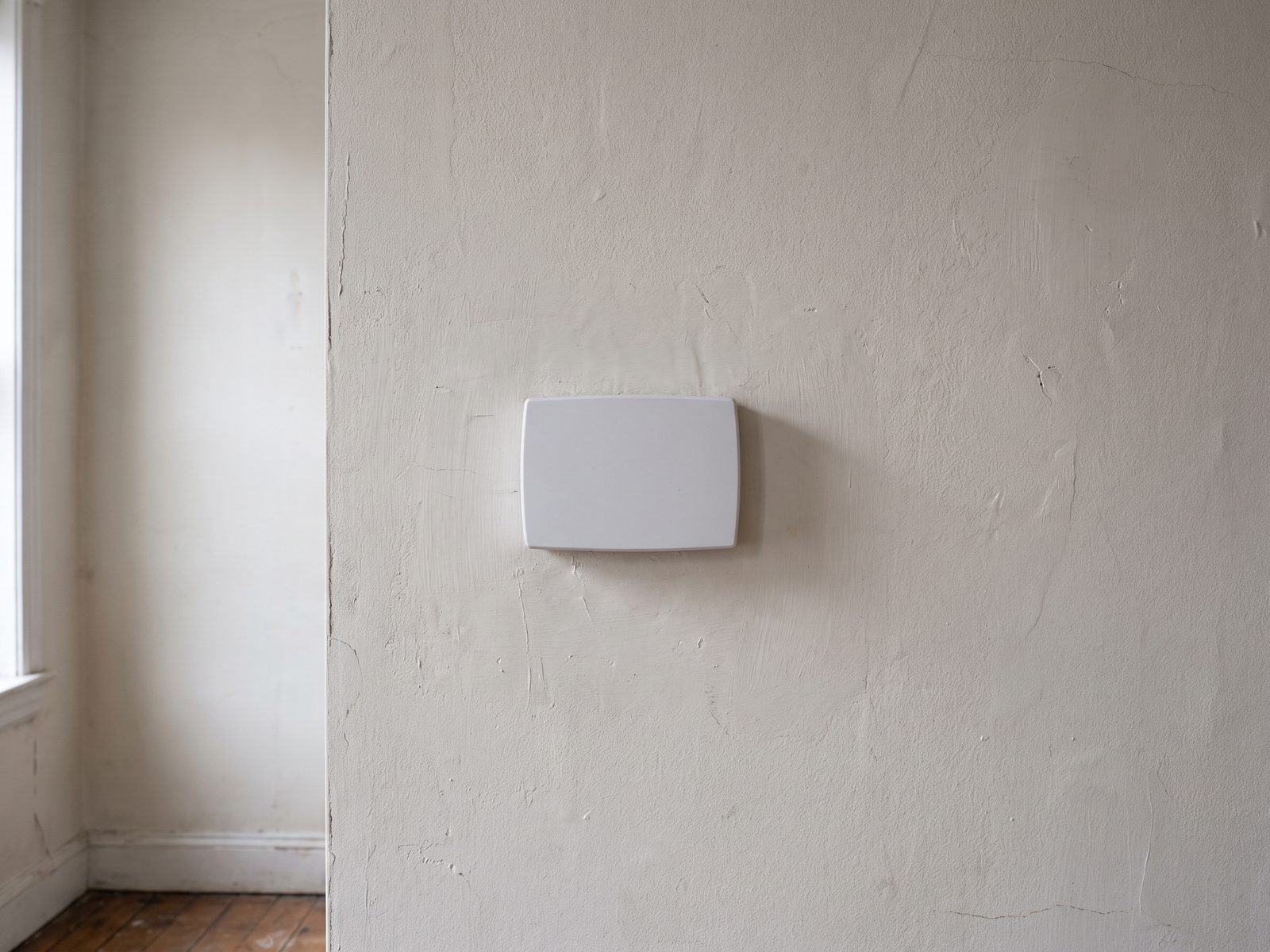 Wall control in an empty room Blank wall-mounted control on a plaster wall in an empty room, winter daylight falling from a window to the left.