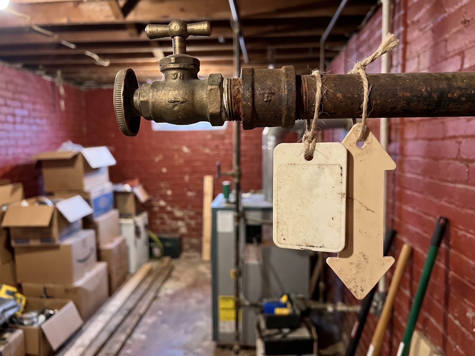 Tagged shutoff valve on a basement pipe Blank tags tied to a basement water pipe next to a shutoff valve, with utility clutter softly out of focus behind.