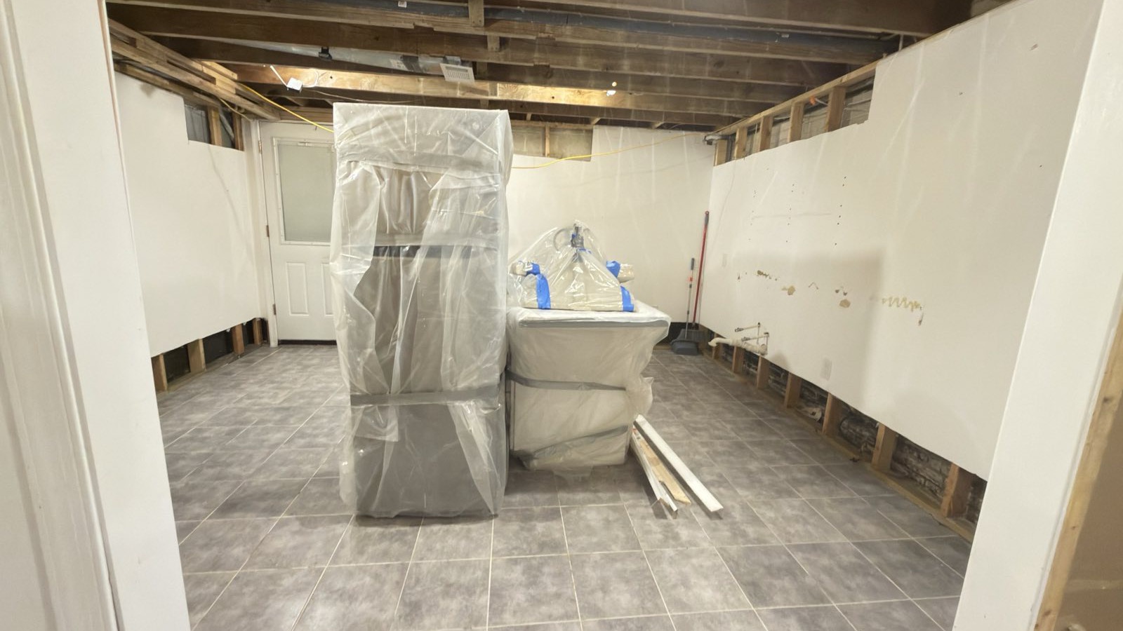 Basement with drywall cut away at the base of the walls and appliances sealed in plastic sheeting