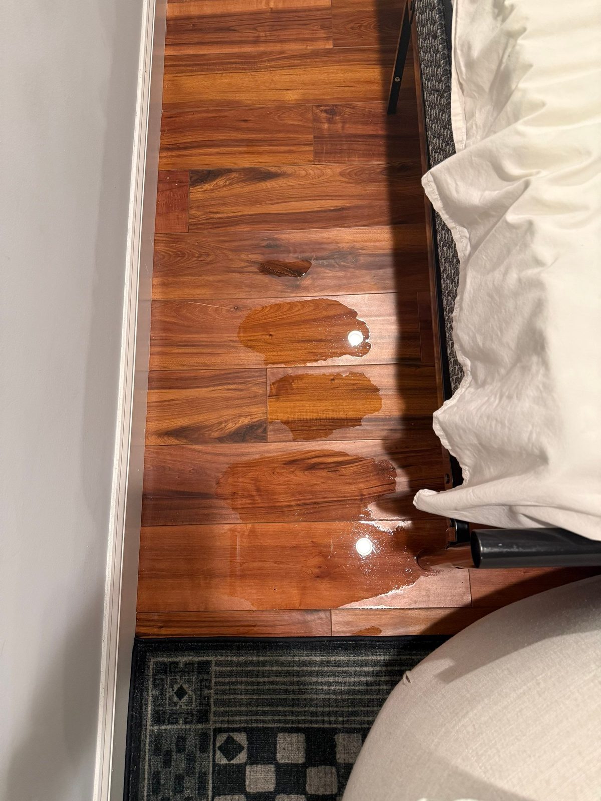 Beads and patches of water on a dark-stained wood floor beside a bed in Washington, DC, July 2025