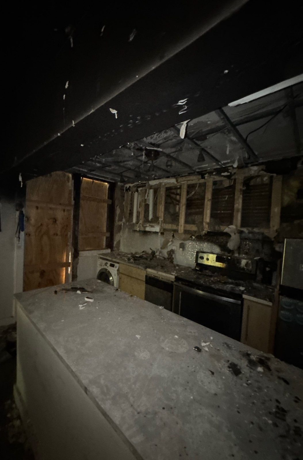 Kitchen with a burned ceiling opened to the framing and soot on the counter in a fire-damaged apartment in Washington, DC, August 2025