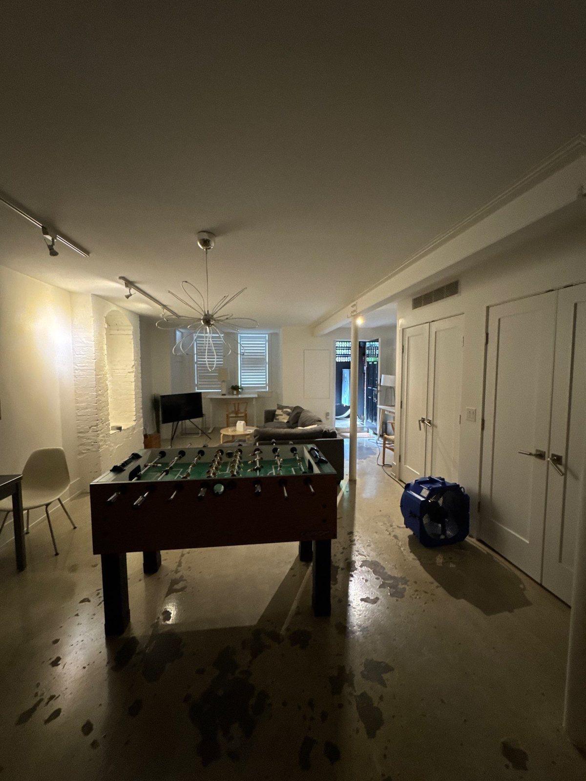 Living area of a garden-level apartment in Shaw, Washington, DC, with an air mover on a wet polished concrete floor, July 2025