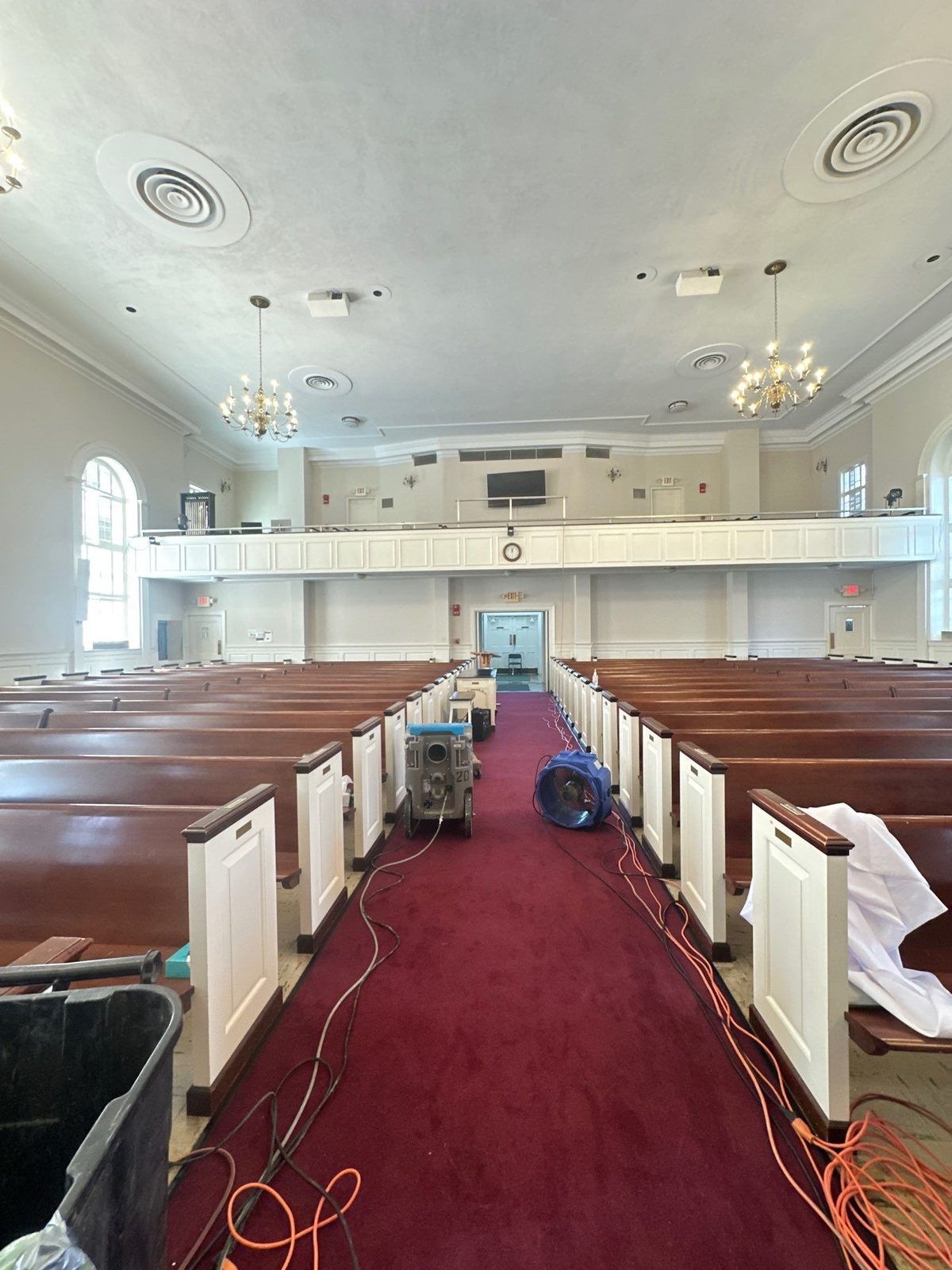 Air mover and dehumidifier on the red carpet of a center aisle between wood pews in a sanctuary in Washington, DC, March 2025