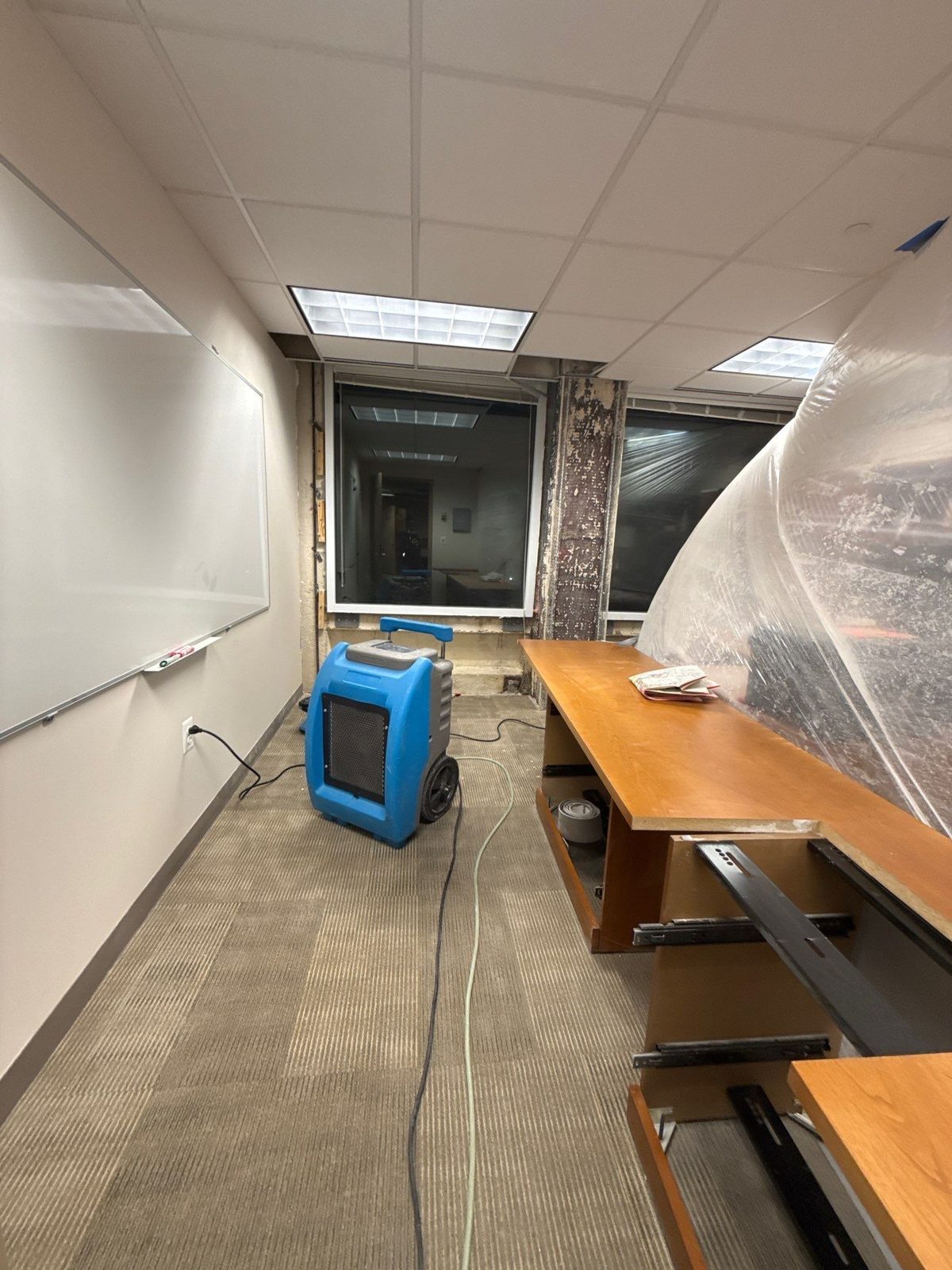 Blue dehumidifier and plastic containment sheeting in an office room with cut-away wall framing in a multi-floor office building in Washington, DC, December 2024
